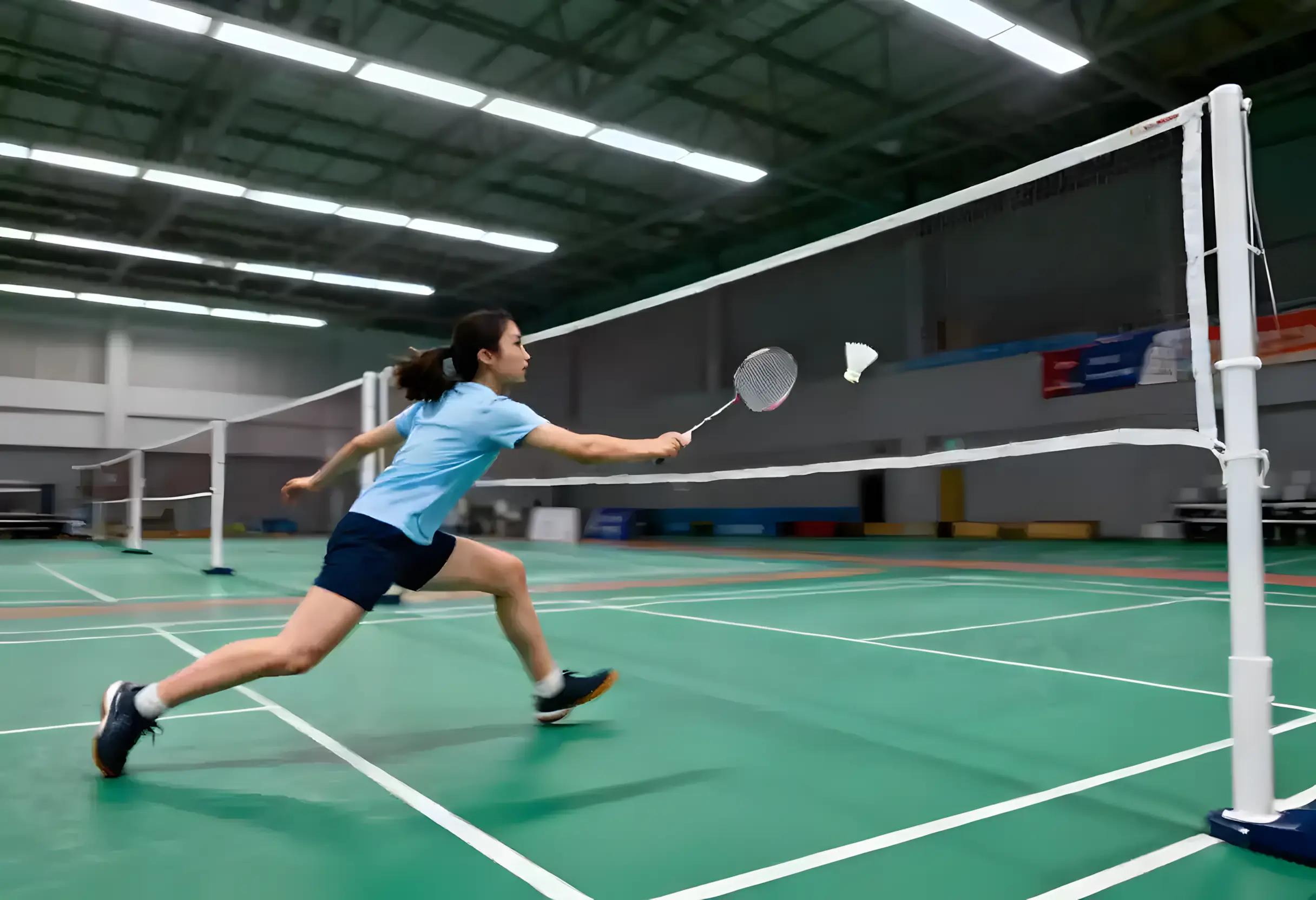 Badminton-Spielerin am Netz während eines Rally-Ballwechsels in einer Sporthalle